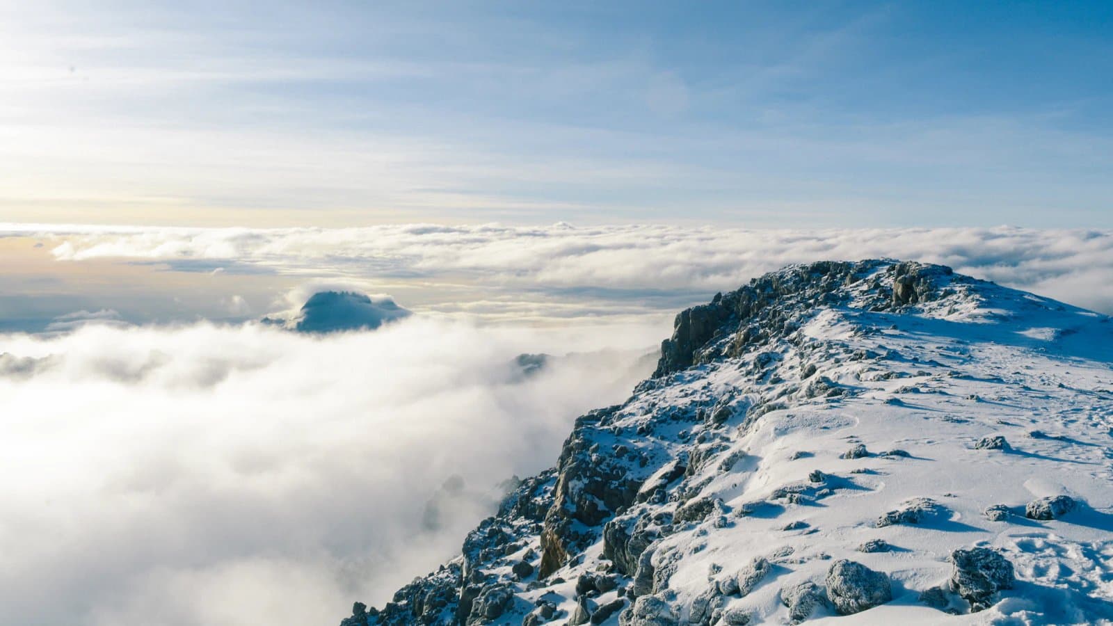 A rocky, snow-covered ridge rising above a sea of clouds